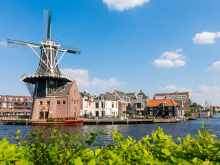 Fototapeta na wymiar Windmill Adriaan and people on waterfront cafe alongside Spaarne river in Haarlem, Holland, Netherlands