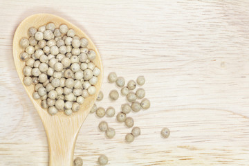 White peppercorn in wooden spoon on nature wood background.