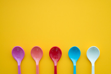 Colorful spoons on yellow background - Kitchen accessories or dishware concept.