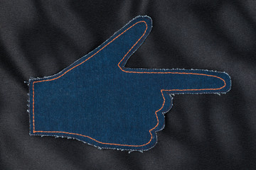 Hand in the shape a pointer made of denim jeans on black satin