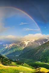 Rainbow under mountain ridge. Panoramic landscape in the summer time