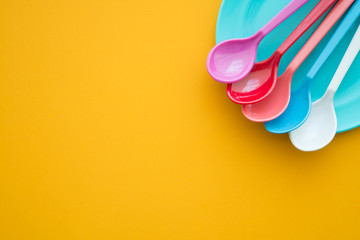 Colorful spoons and plate on yellow background - Kitchen accessories or dishware concept.