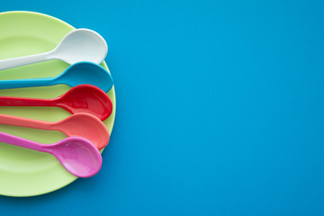 Colorful spoons and plate on blue background - Kitchen accessories or dishware concept.