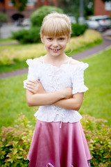 Portrait of beautiful little girl in a white blouse with a pink skirt in the Park