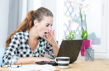 Tired woman yawning during working in home office using laptop