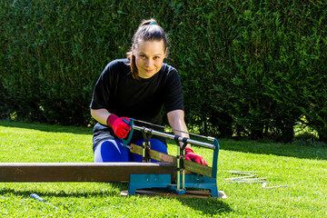 Girl is sawing a wooden beam in the garden
