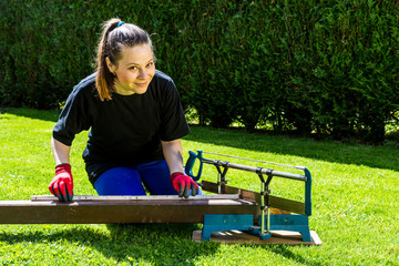 Girl is sawing a wooden beam in the garden