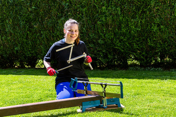 Girl is sawing a wooden beam in the garden