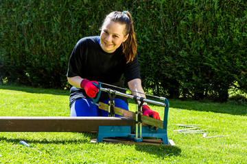 Girl is sawing a wooden beam in the garden