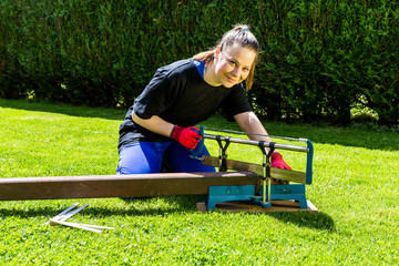 Girl is sawing a wooden beam in the garden