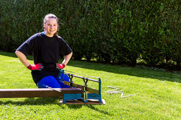 Girl is sawing a wooden beam in the garden