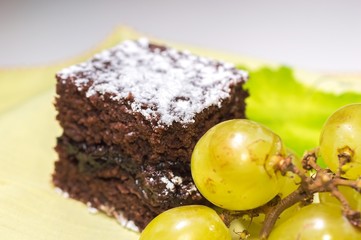 Chocolate sponge cake with icing sugar and grapes on the yellow tablecloth