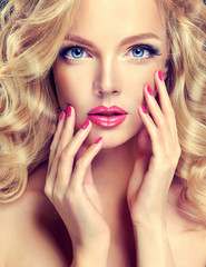 Beautiful blonde model with long curly hair .  Girl with blue eyes and  pink manicure on nails