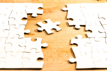 finishing the puzzle, white jigsaw/puzzle whit one gap, over  a wooden table background, symbol of problem solving