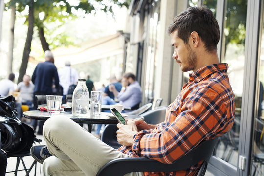 Attractive Man Sitting In Cafe Bar And Holding Mobile Smart Phone