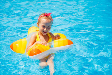 Portrait of cute happy little girl having fun in swimming pool, floating in blue refreshing water with big rubber ring, active summer vacation on the beach