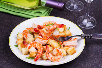 Shrimp with crispy croutons and scallions in white plate. White wine bottle