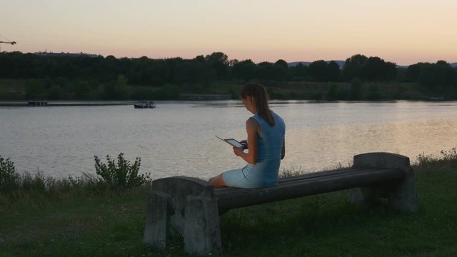 Young woman reads an e-book at sunset in the park