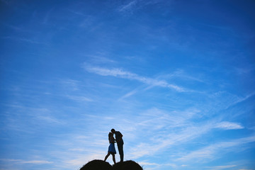 silhouette of a couple kissing on a haystack on blue sky with clouds