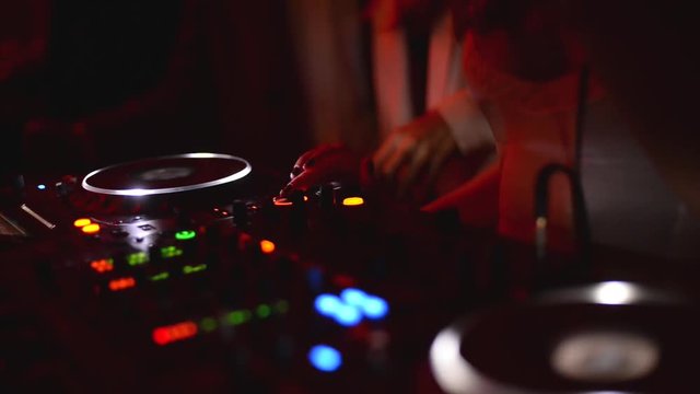 Women's hands tweak various controls on dj's deck