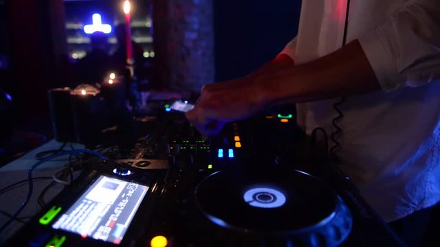Hands of male Dj tweak various controls on dj's deck