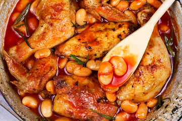 Chicken and white bean in tomato sauce with rosemary in frying pan on white wooden background