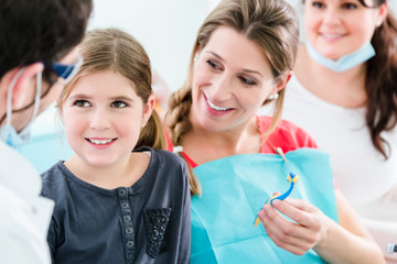 Zahnarzt mit schwangerer Frau und Kind in Praxis samt Sprechstundenhilfe