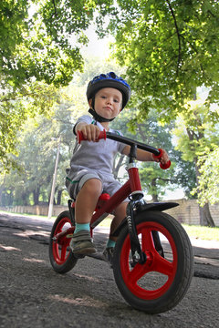 Little White Toddler Cyclist In The Protective Helmet Rides On A