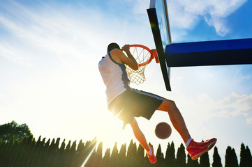 Street basketball player performing power slum dunk.