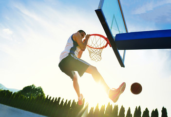 Street basketball player performing power slum dunk.
