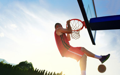 Young basketball player drives to the hoop for a high flying slam dunk in front of sunset sky.