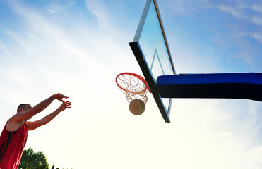Young basketball player drives to the hoop for a high flying slam dunk in front of sunset sky.