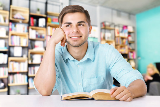 Young man with book on blurred book shelves background.