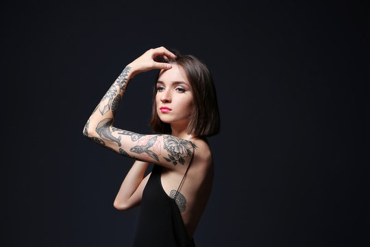 Beautiful young woman with tattoo posing on black background
