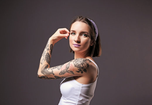 Beautiful young woman with tattoo posing on gray background