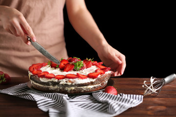 Obraz na płótnie Canvas Woman slicing appetizing cake decorated with strawberry