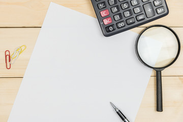 Top view of blank paper on wooden desk with magnifying glass and calculator.