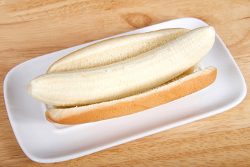 Banana in a hot dog bun served on a white rectangular plate served on a wood table. Top view from an angle