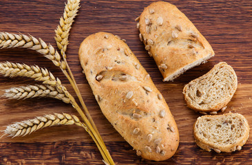 Loaf of bread, bread slices and wheat over wooden background