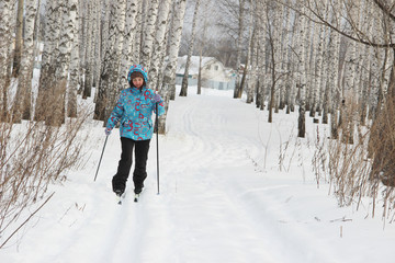 a girl in a blue jacket is skiing in the winter snowy forest