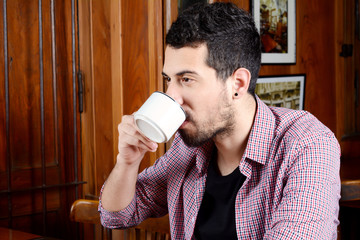 Young latin man drinking coffee at a cafe.