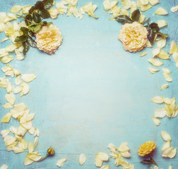 Yellow roses with petals on turquoise blue shabby chic  background, top view, frame.