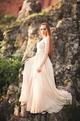 Fototapeta premium Attractive young woman in long dress standing on the rocks