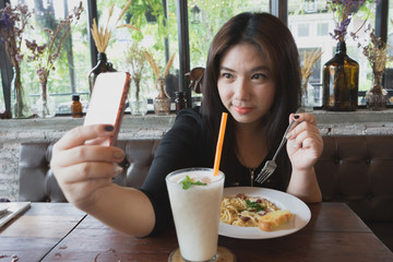 woman look at mobile phone social network take selfie photo picture with lychee juice and carbonara spaghetti at restaurant with wooden table and relax atmosphere