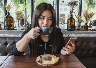 A woman is sipping coffee with looking at mobile phone social network at coffee time with wooden table and relax atmosphere