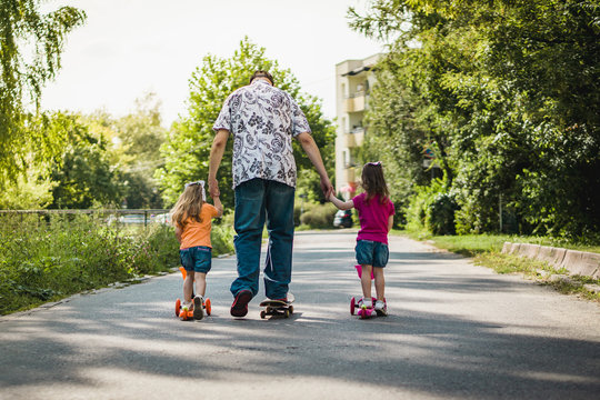 Dad With His Daughters On A Skateboard And Scooter