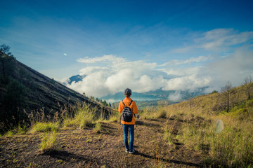 Naklejka premium Young woman with backpack standing on cliff's edge and looking to a sky