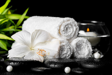 spa still life of white hibiscus flower, bamboo, towels and round vase with candle, pearl beads on zen basalt stone with drops