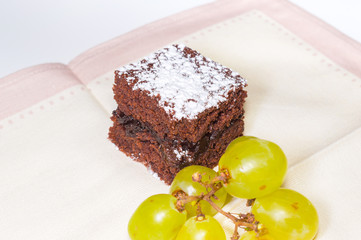 Chocolate sponge cake with icing sugar and grapes on the beige tablecloth