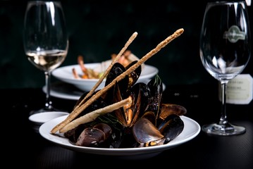 Mussels on a white plate with a glass of wine in a restaurant, side view.